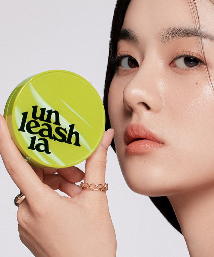 A woman holding a UNLEASHIA Satin Wear Healthy Green Cushion compact, highlighting the product's sleek design and vibrant green color.