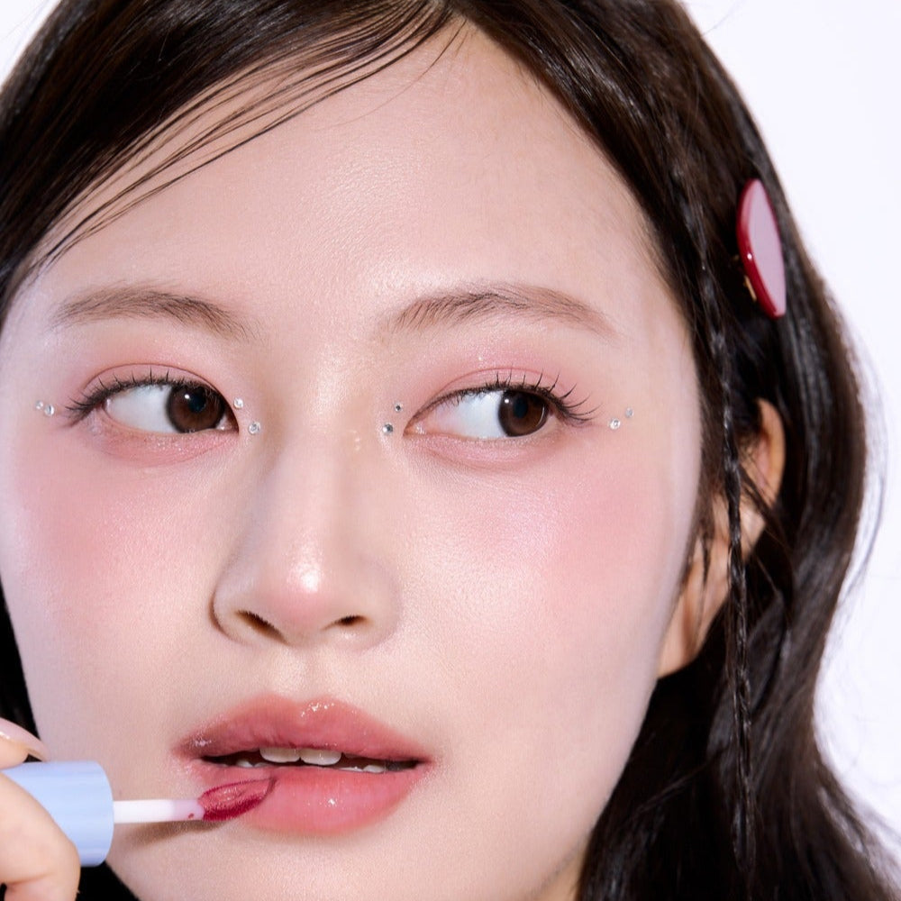 Woman applying lipstick with UNLEASHIA Tanghulu Glaze Tint, close-up shot showing glossy finish and vibrant color.