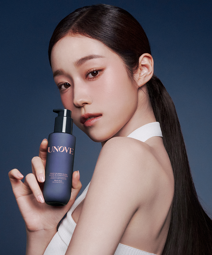 Model holding UNOVE Frizz Calming Sleek Leave-In Conditioner 150ml bottle against a dark background