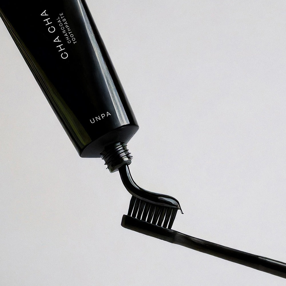 UNPA Cha Cha Charcoal Original Toothpaste 100g being squeezed onto a black toothbrush
