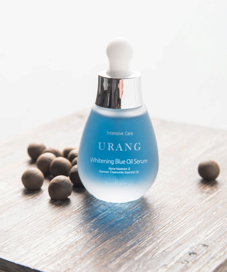 URANG Brightening Blue Oil Serum 30ml on wooden surface with scattered brown nuts