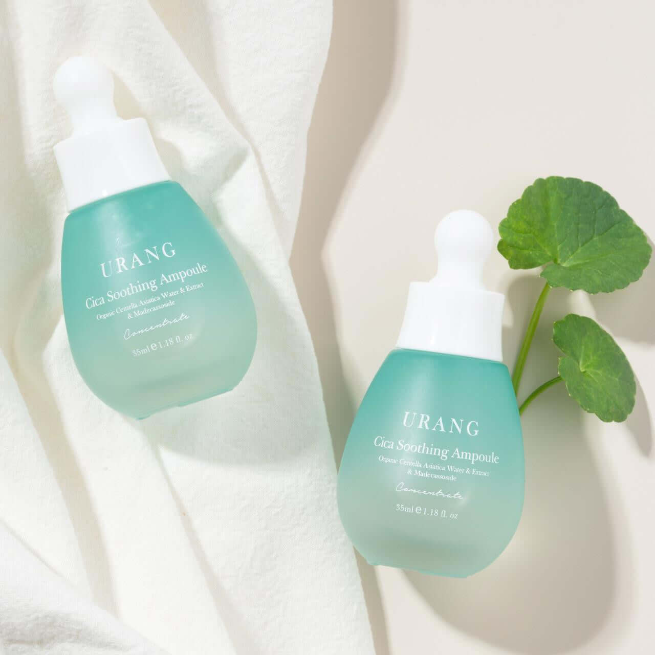 URANG Cica Soothing Ampoule bottles on white fabric with green leaves