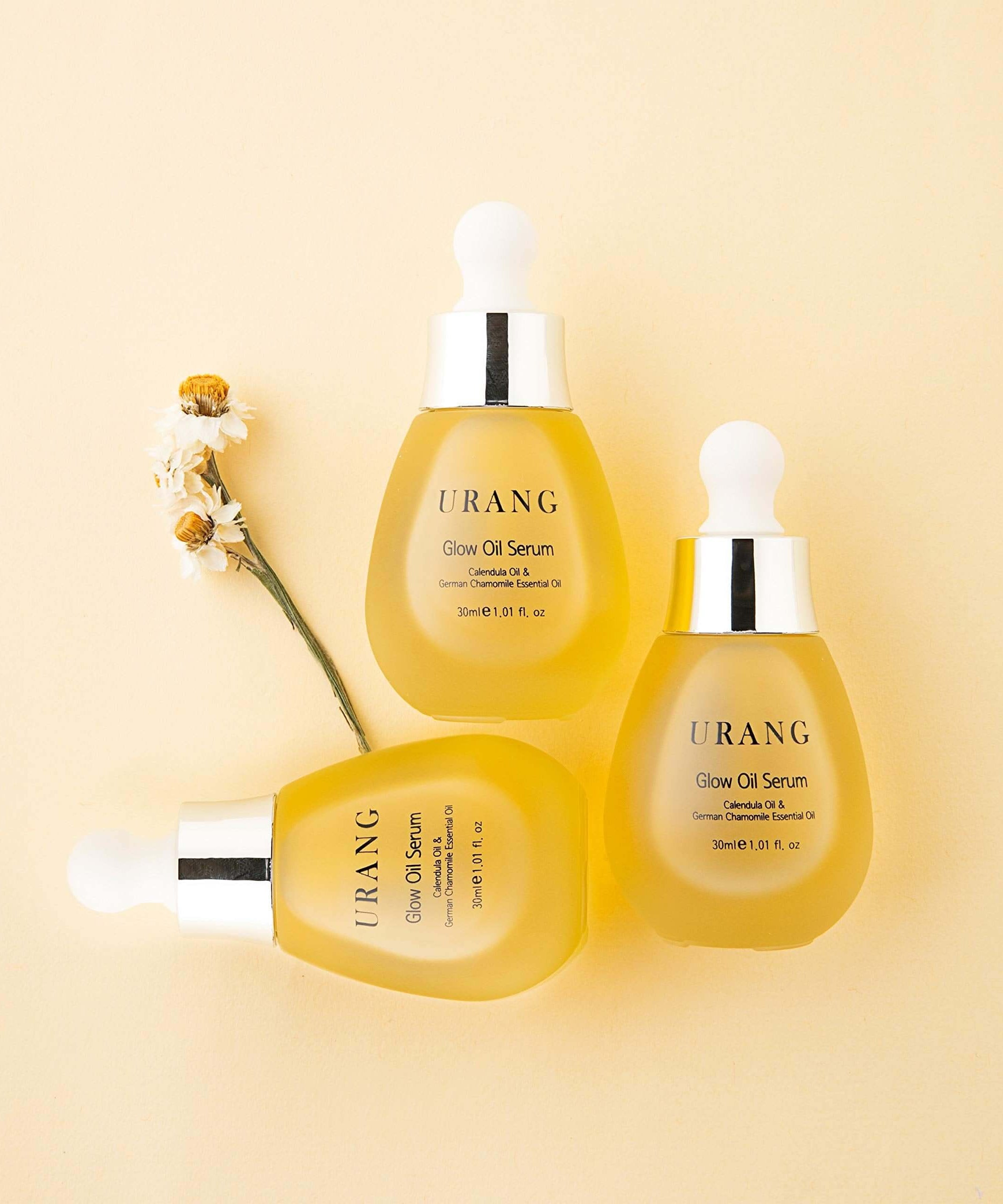 URANG Glow Oil Serum 30ml bottles displayed on a soft yellow background with floral accents