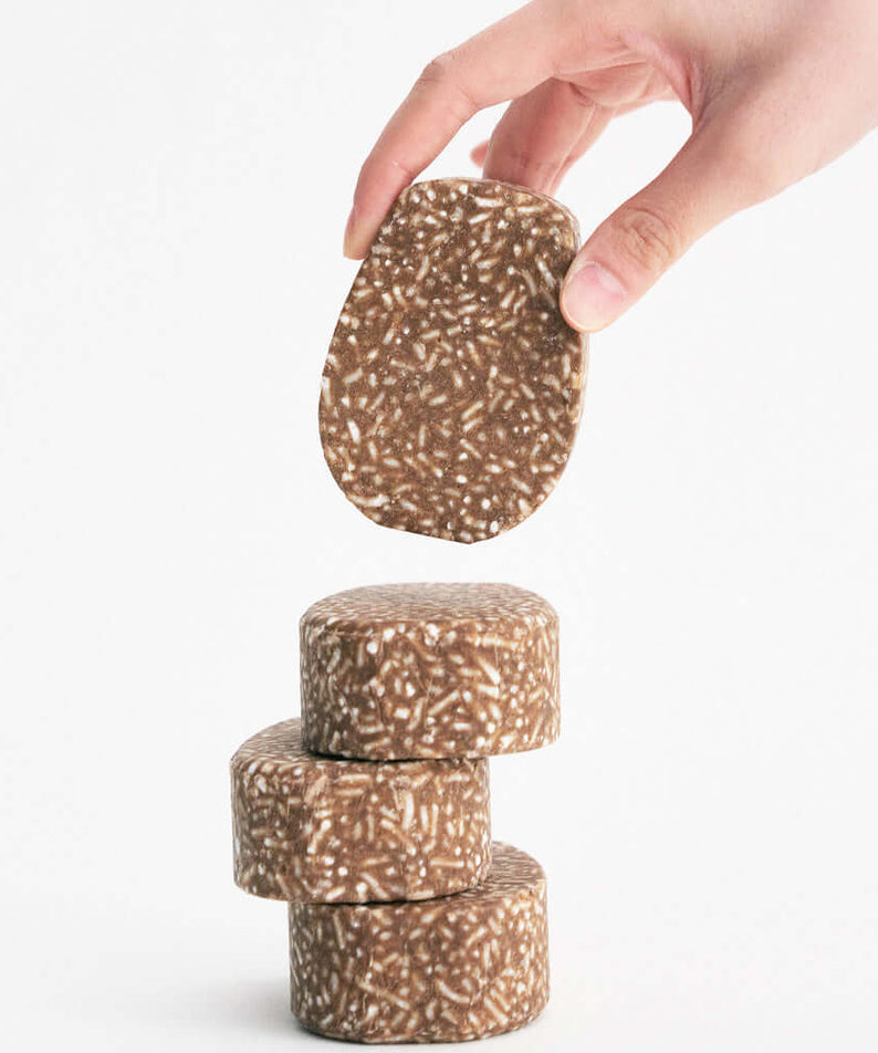 URANG Mugwort Calming Shampoo Bar being held above a stack of similar bars on white background