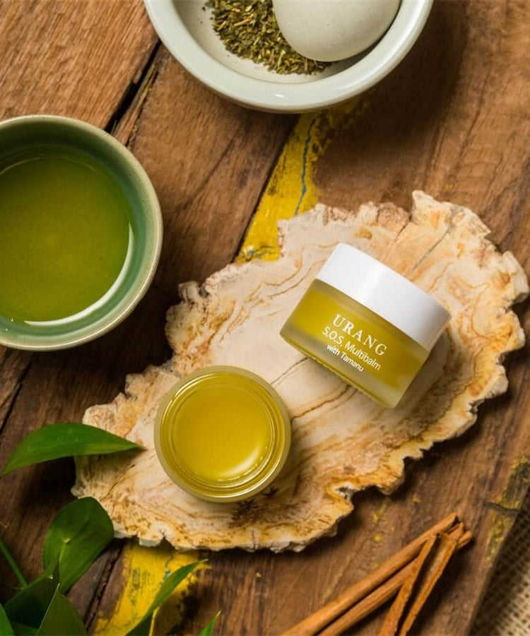 Image of URANG SOS Multi Balm jar with natural ingredients on a rustic wooden surface, showcasing the skincare product's natural appeal.