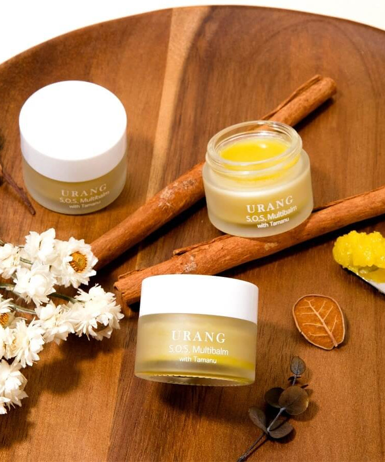 URANG SOS Multi Balm on a wooden tray with cinnamon sticks and flowers; moisturizing skincare balm with tamanu oil.