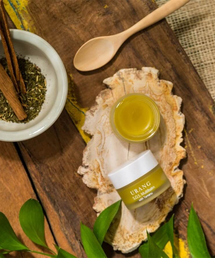 URANG SOS Multi Balm on wooden surface with herbs and spoon