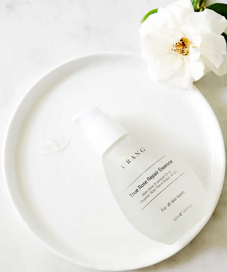 URANG True Rose Repair Essence displayed on a white plate with a white rose, highlighting premium skincare.