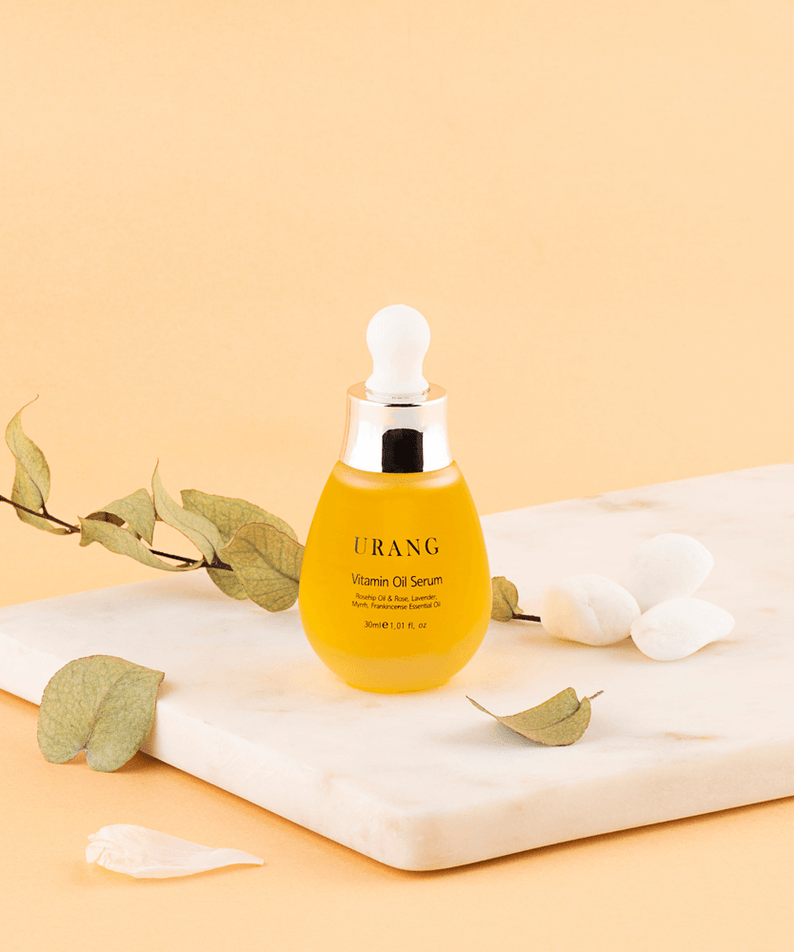 URANG Vitamin Oil Serum 30ml on marble surface with leaves and petals, highlighting luxurious skincare product