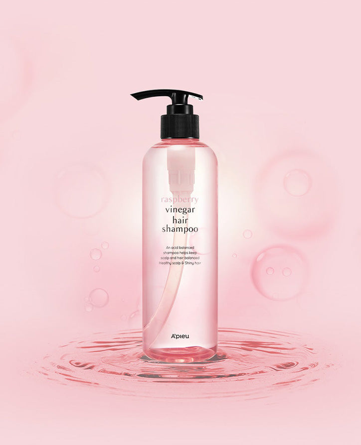 A bottle of raspberry vinegar hair shampoo by A'pieu, placed against a pink background with water ripples and bubbles.