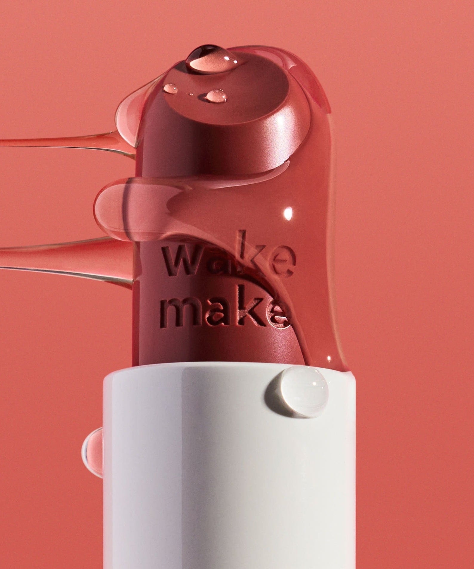 WAKEMAKE Healthy Glow Balm Sticks in a sleek tube with glossy pink balm on a coral background
