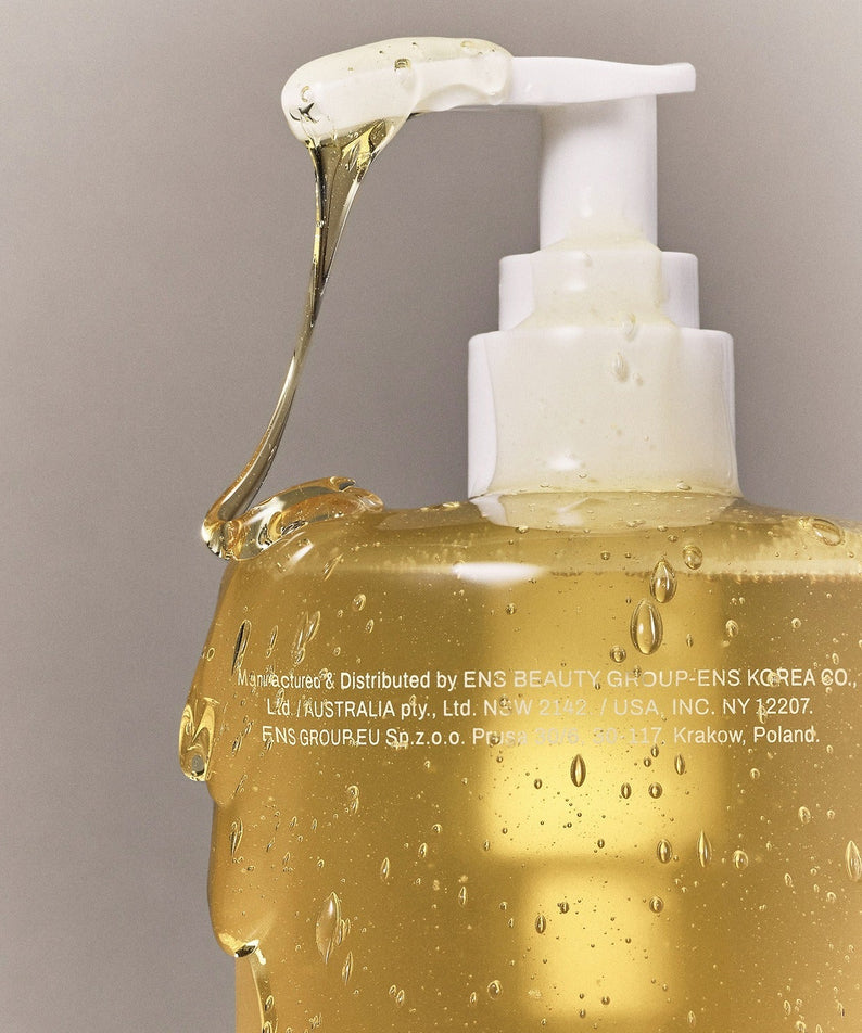 Close-up of WHAMISA Organic Seed Fermented Body Cleanser 490ml bottle with pump dispenser, showing golden liquid texture and design.
