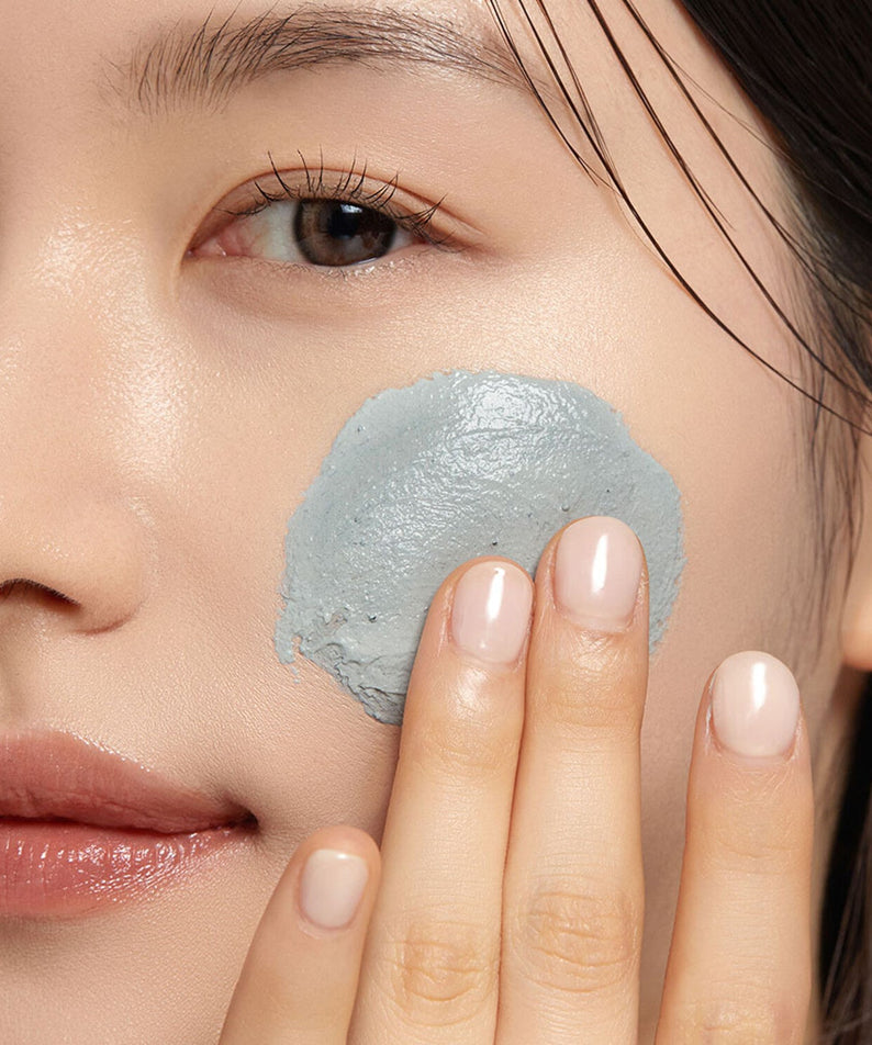 Woman applying WHIPPED Mugtree Vegan Cookie Clay Pack Cleanser 180ml on her cheek for skincare routine.
