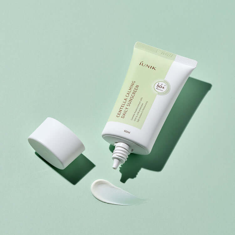 iUNIK Centella Calming Daily Sunscreen 60ml tube on a green background with opened cap and swatch of sunscreen.
